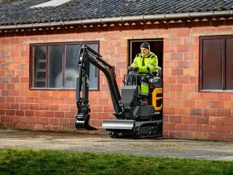 hyundai-hx10a-z-compact-excavator-Compact excavator with operator in neon hi-vis working beside a brick building with windows and open doorway